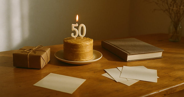A milestone birthday table with a lit candle cake, a wrapped gift, a closed photo album and face-down old prints